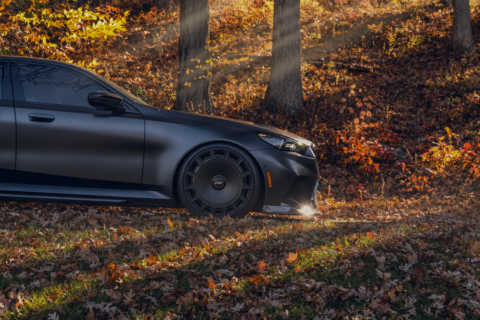 Black luxury car equipped with LSW forged wheels parked in golden autumn forest